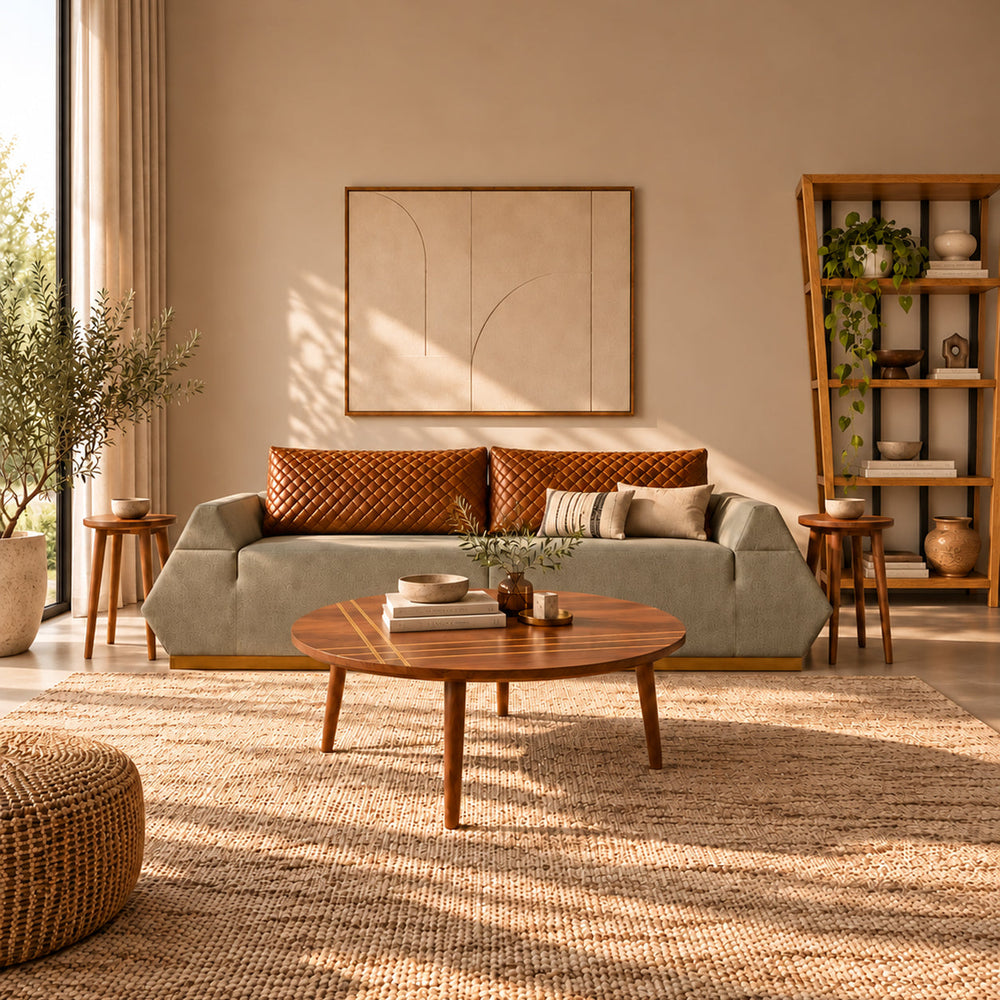 Sunlit lounge with grayish Pyra sofa and havane leather cushions, round wooden coffee table, two side tables and oak shelving.